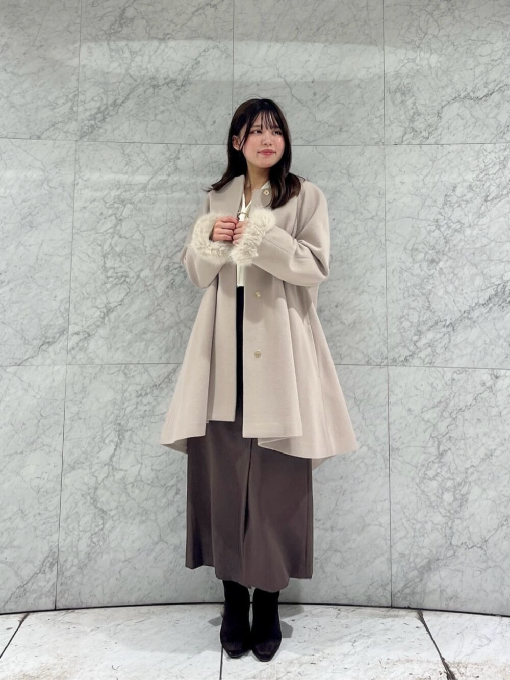 ホワイト系のニット/セーター、ベージュ系のノーカラーコート、ブラウン系のスカートを着用したレディースの秋コーディネートの2枚目の写真
