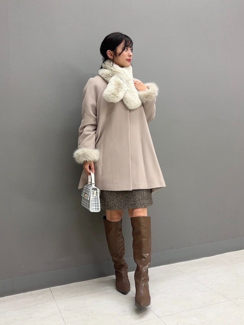 ホワイト系のショルダーバッグ、ブラウン系のブーツ、ベージュ系のノーカラーコートを着用したレディースの冬コーディネートの2枚目の写真