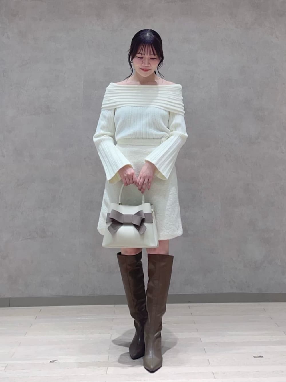 ベージュ系のショルダーバッグ、ホワイト系のスカート、ブラウン系のブーツを着用したレディースの冬コーディネートの2枚目の写真