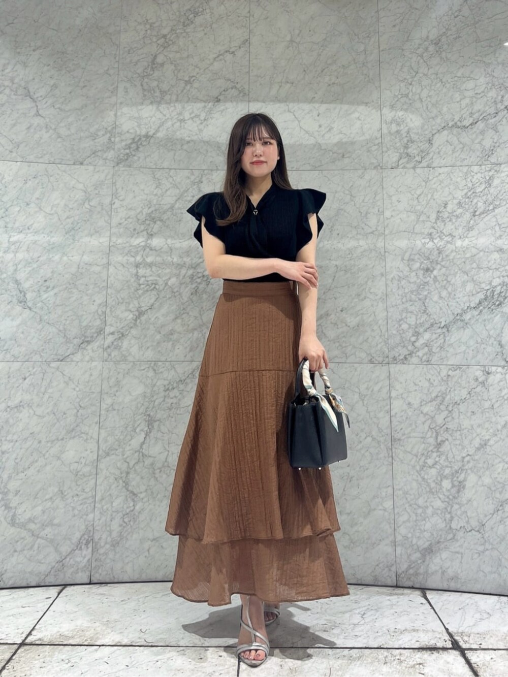 シルバー系のパンプス、ブラック系のニット/セーター、ブラウン系のスカートを着用したレディースの夏コーディネートの2枚目の写真