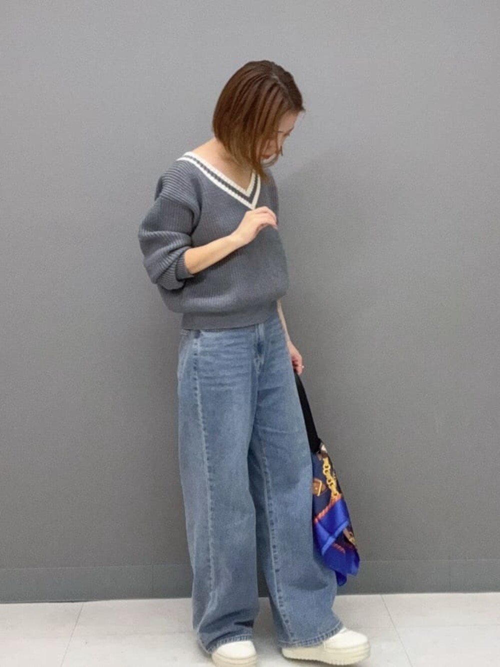 グレー系のニット/セーター、ブルー系のデニムパンツ、ブラック系のハンドバッグを着用したレディースの秋コーディネートの2枚目の写真