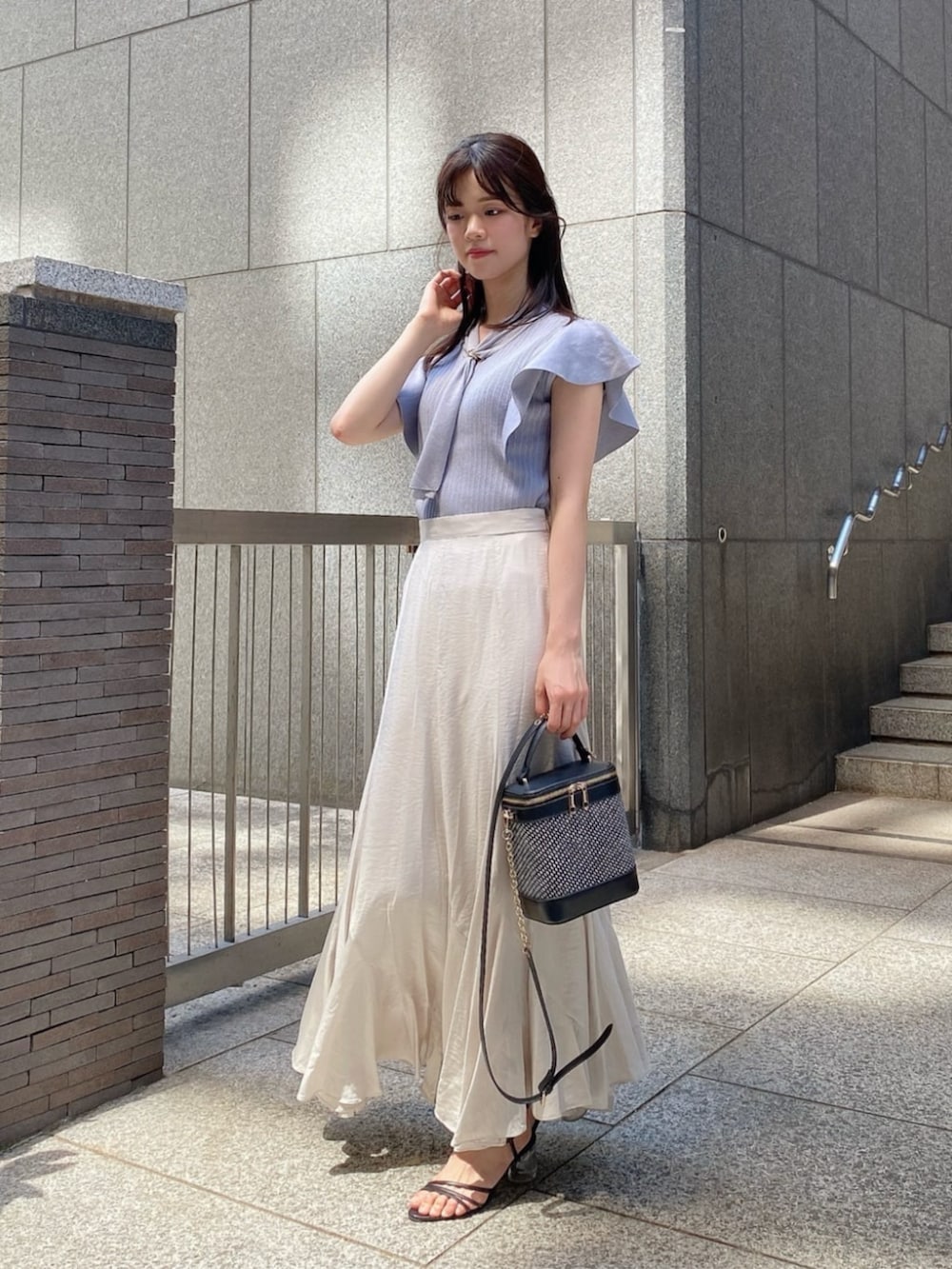 ブラック系のショルダーバッグ、ブルー系のニット/セーター、グレー系のスカートを着用したレディースの夏コーディネートの2枚目の写真