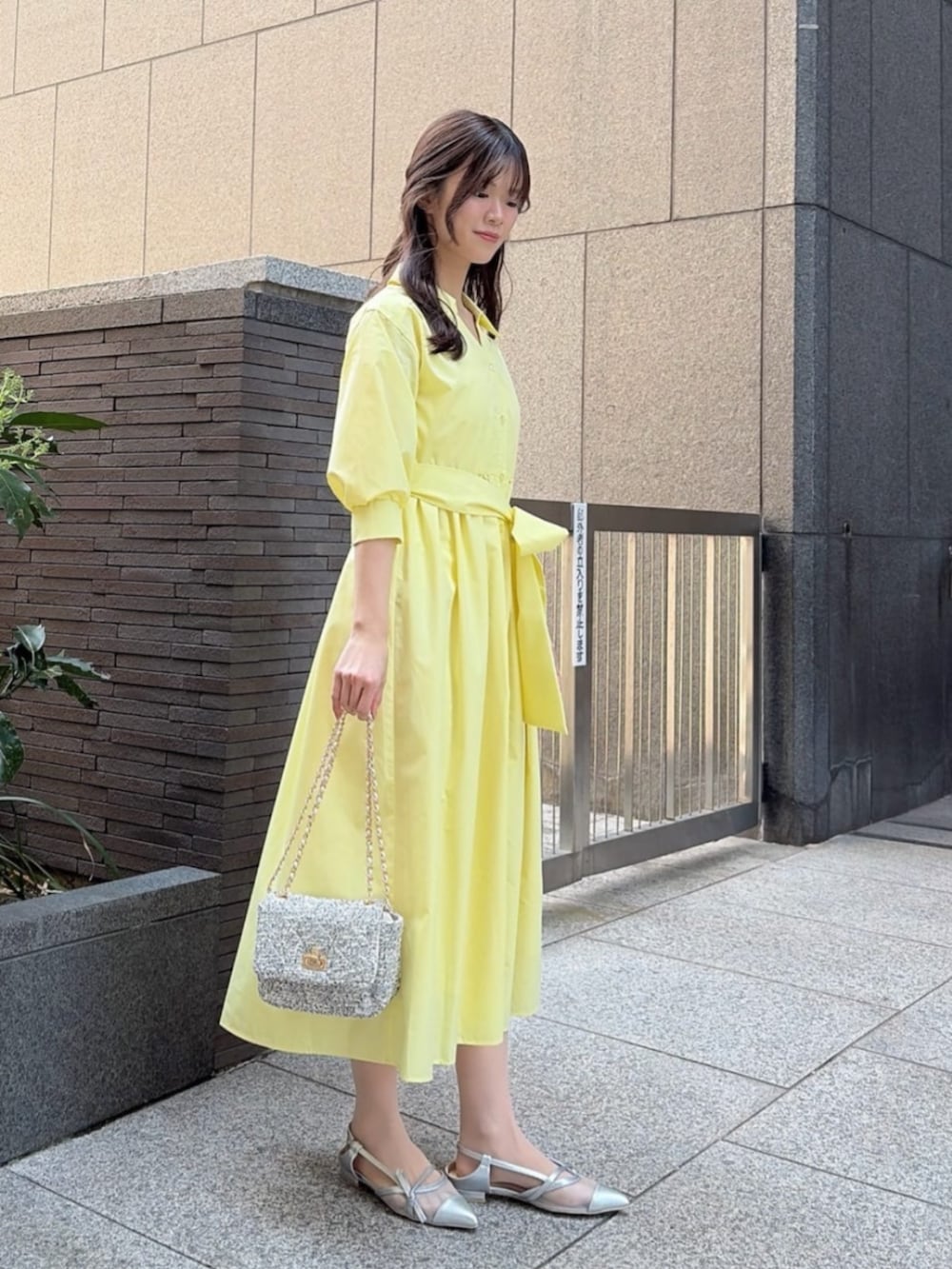 ブラック系のショルダーバッグ、イエロー系のワンピース、シルバー系のパンプスを着用したレディースの春コーディネートの2枚目の写真