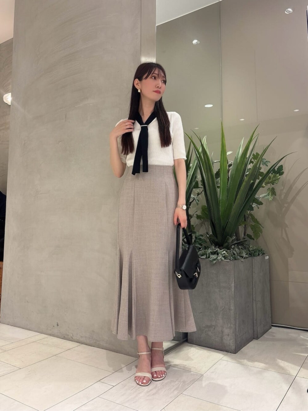 ブラック系のショルダーバッグ、ブラウン系のスカート、ホワイト系のニット/セーターを着用したレディースの夏コーディネートの2枚目の写真