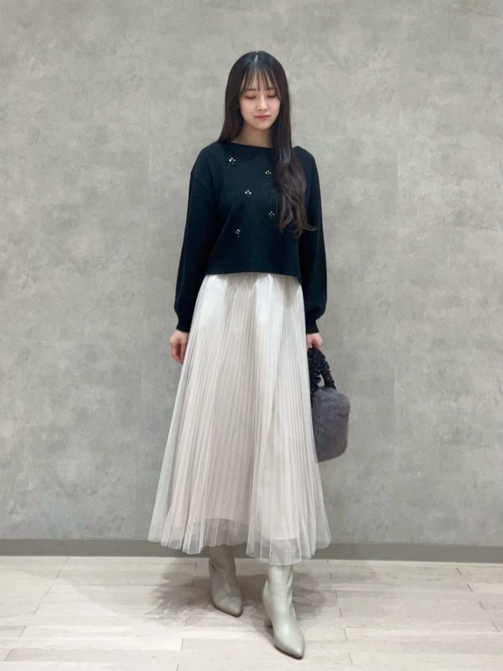 グレー系のトートバッグ、ブラック系のニット/セーター、ホワイト系のスカートを着用したレディースの冬コーディネートの2枚目の写真