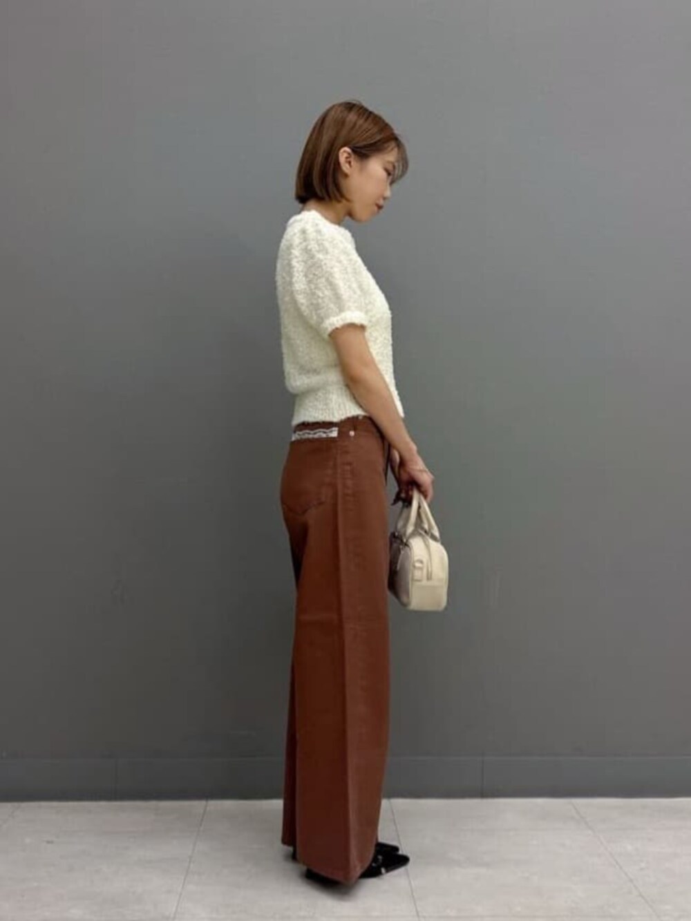 ブラウン系のデニムパンツ、ホワイト系のボストンバッグ、ホワイト系のニット/セーターを着用したレディースの秋コーディネートの2枚目の写真