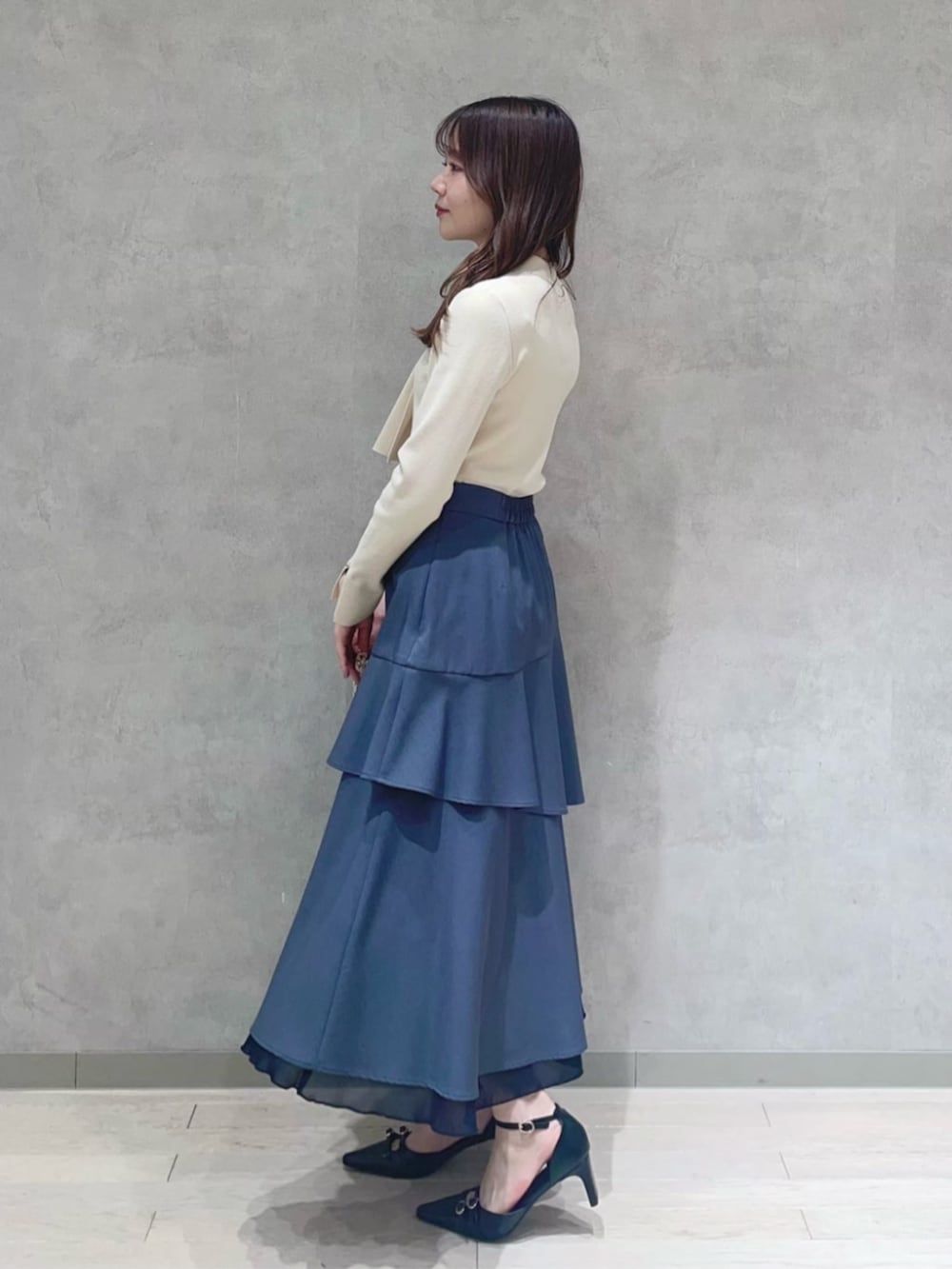 ブルー系のショルダーバッグ、ホワイト系のニット/セーター、グレー系のスカートを着用したレディースの春コーディネートの2枚目の写真