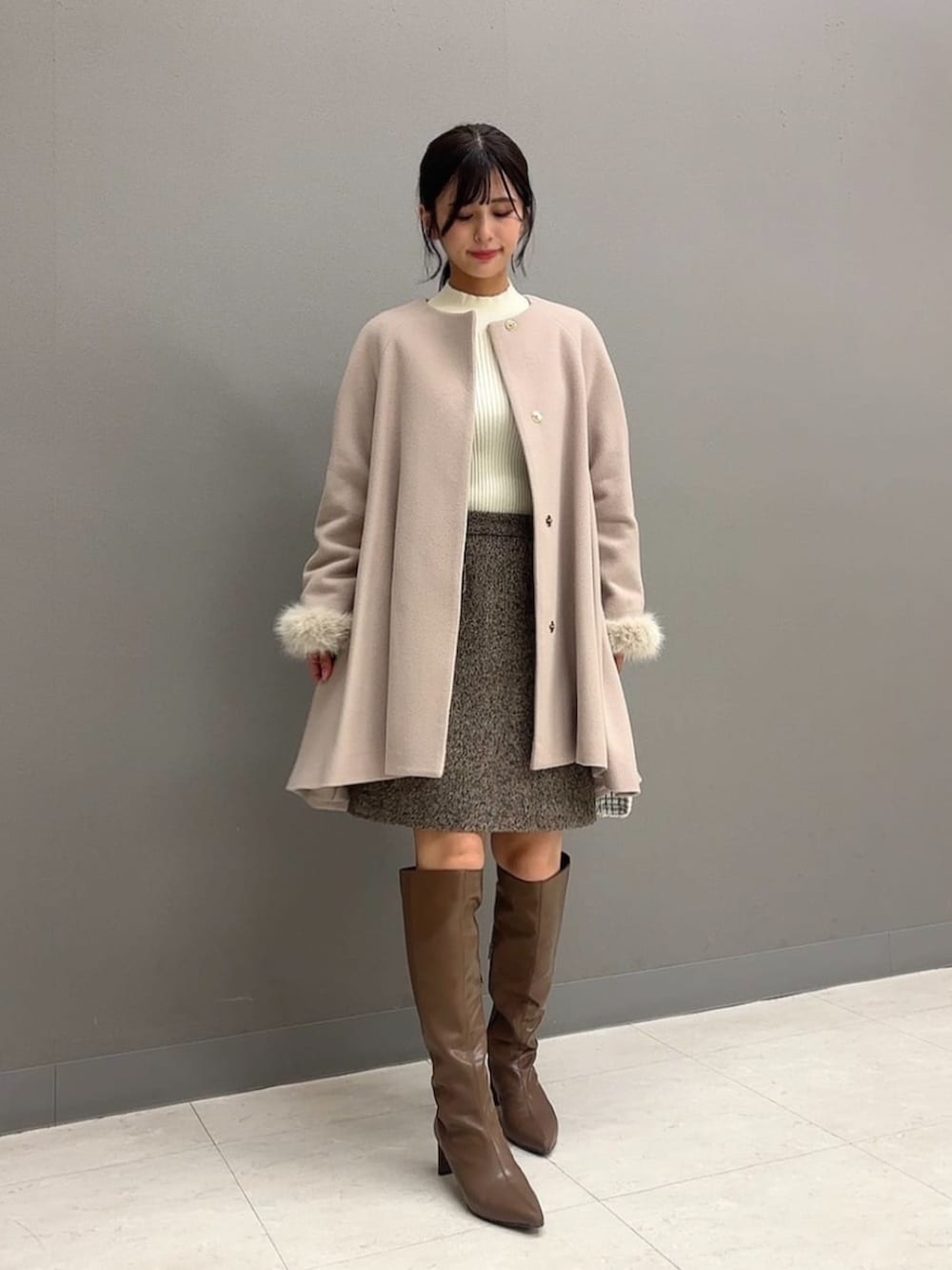 ホワイト系のショルダーバッグ、ブラウン系のブーツ、ベージュ系のノーカラーコートを着用したレディースの冬コーディネートの3枚目の写真