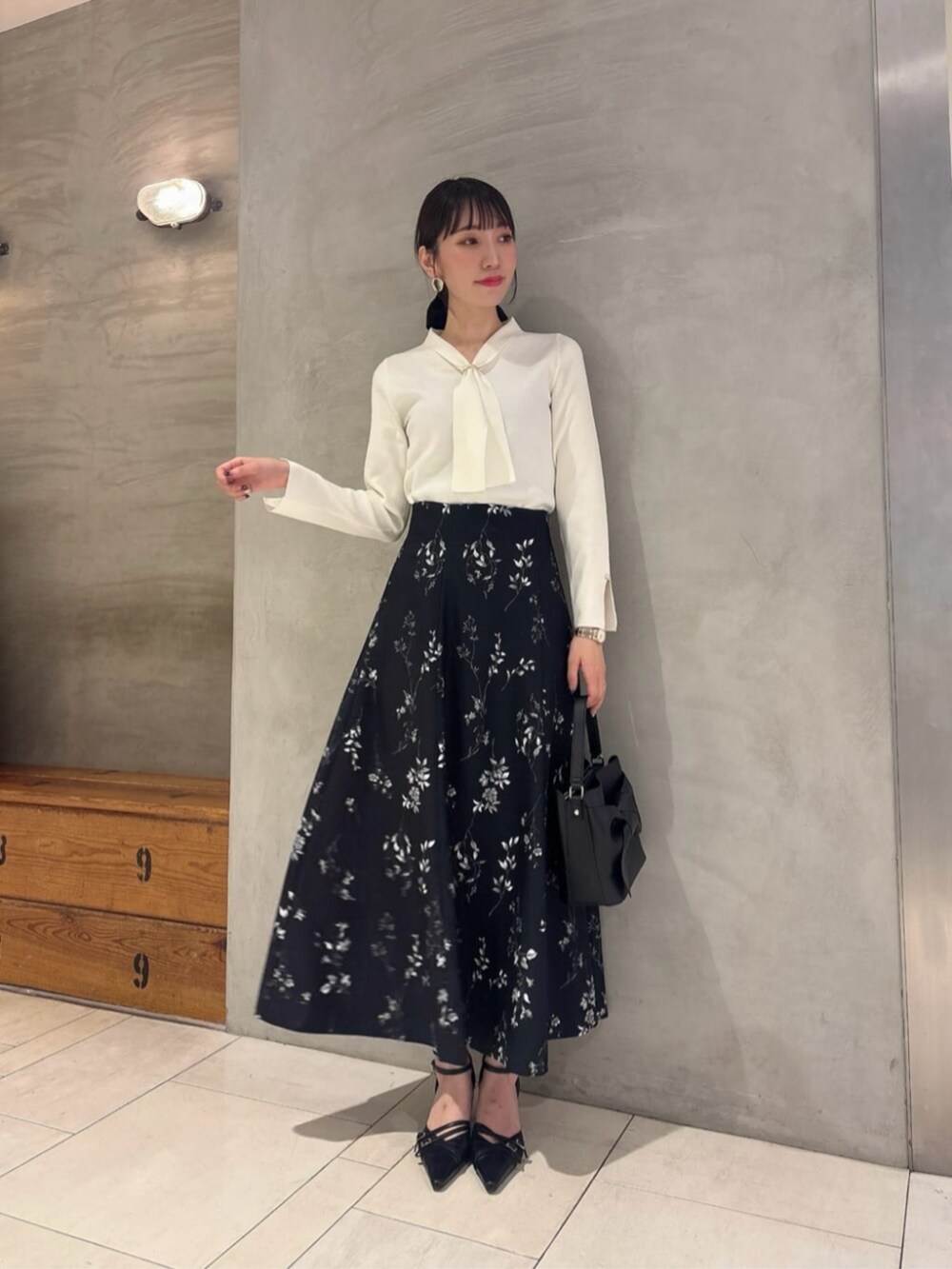 ブラック系のパンプス、ホワイト系のニット/セーター、ブラック系のスカートを着用したレディースの秋コーディネートの2枚目の写真