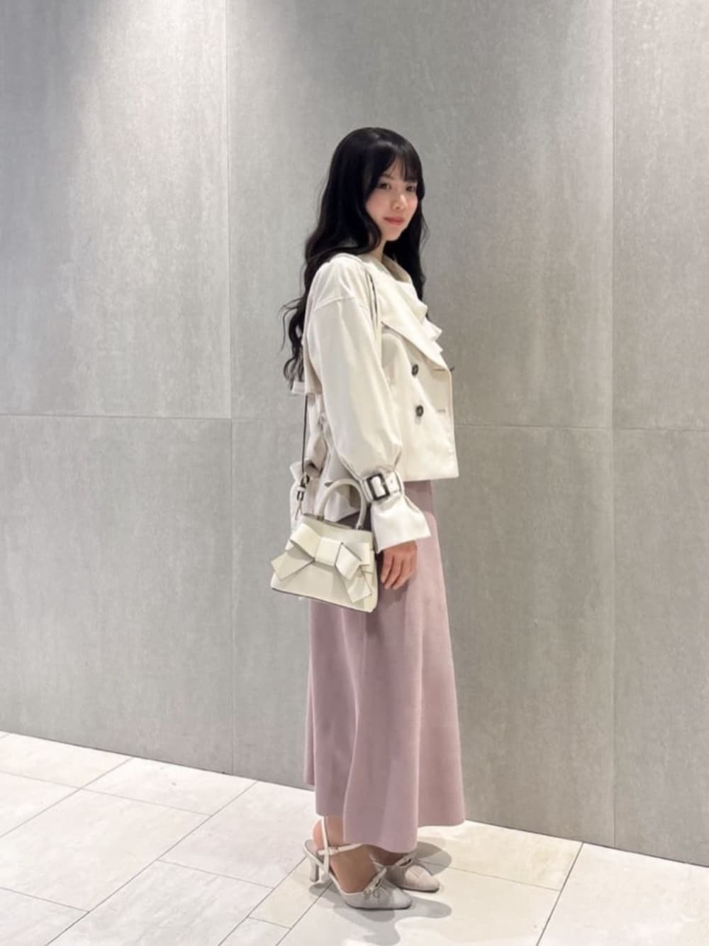 ホワイト系のショルダーバッグ、ベージュ系のトレンチコート、ピンク系のワンピースを着用したレディースの春コーディネートの2枚目の写真