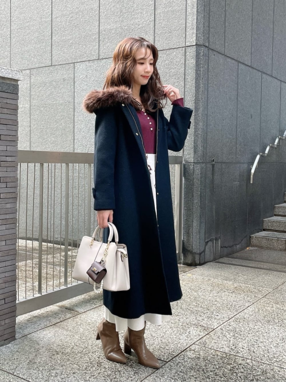 ブラウン系のブーツ、ブラック系のステンカラーコート、レッド系のワンピースを着用したレディースの冬コーディネートの2枚目の写真