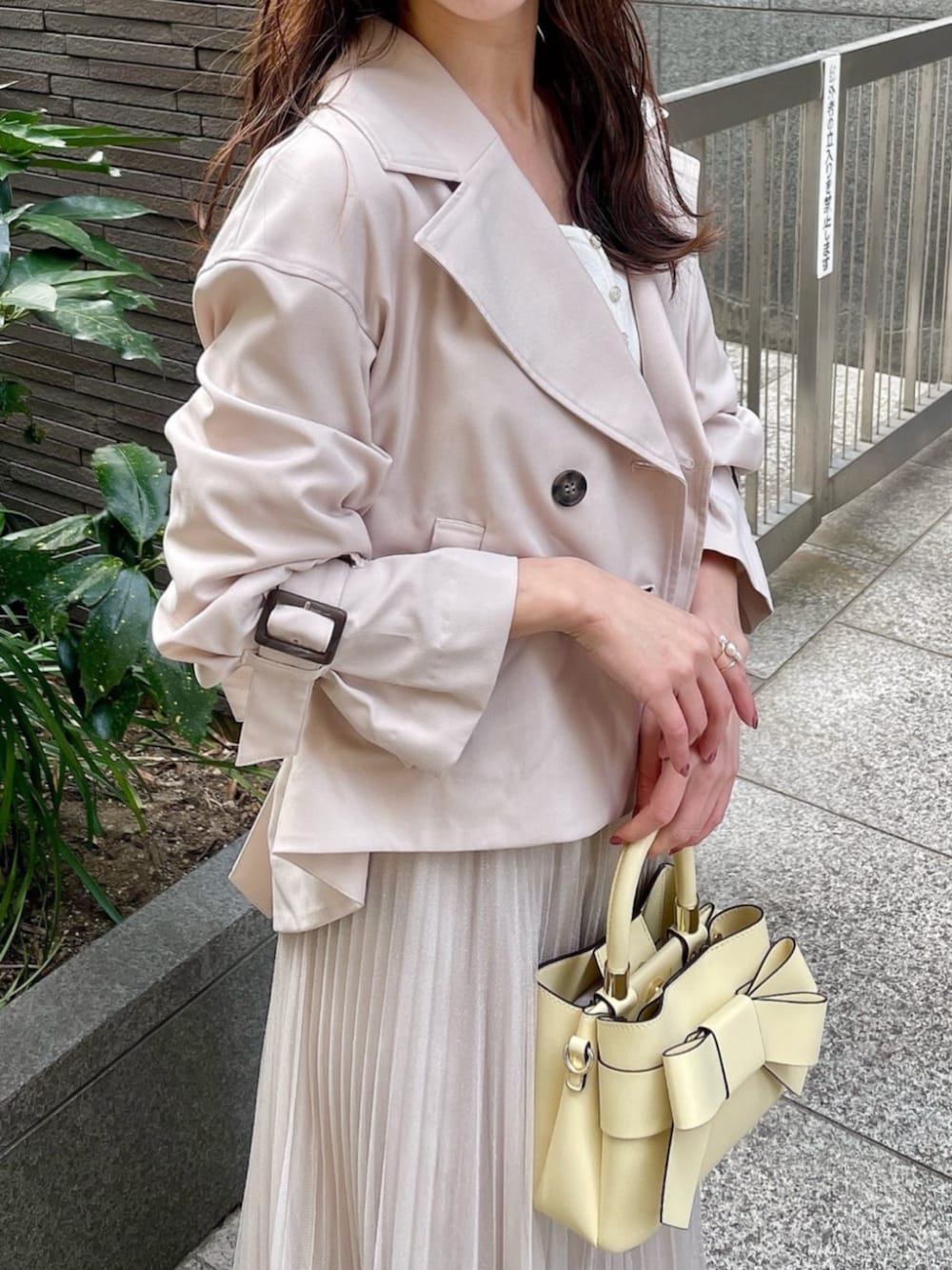 イエロー系のショルダーバッグ、ベージュ系のトレンチコート、ホワイト系のスカートを着用したレディースの春コーディネートの3枚目の写真