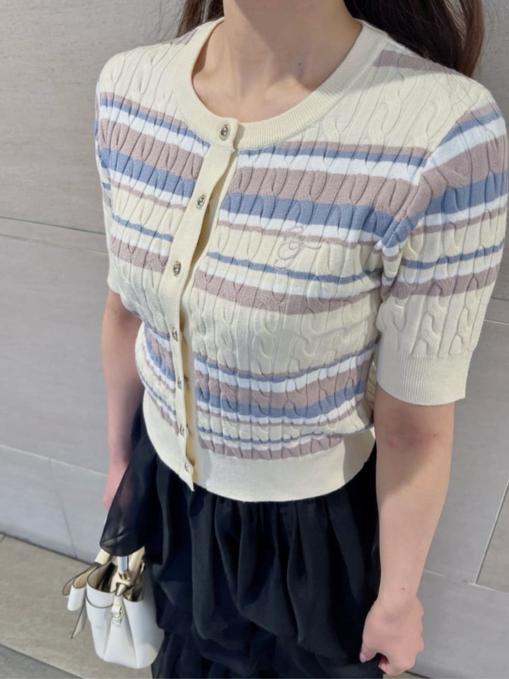 ホワイト系のショルダーバッグ、ホワイト系のカーディガン/ボレロ、ブラック系のスカートを着用したレディースの春コーディネートの3枚目の写真