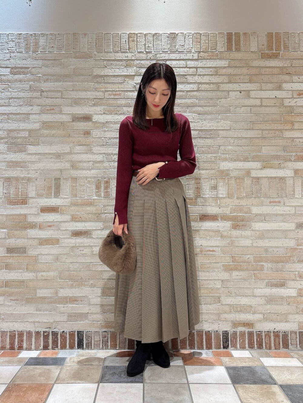 ブラウン系のスカート、レッド系のニット/セーター、ブラウン系のハンドバッグを着用したレディースの秋コーディネートの2枚目の写真