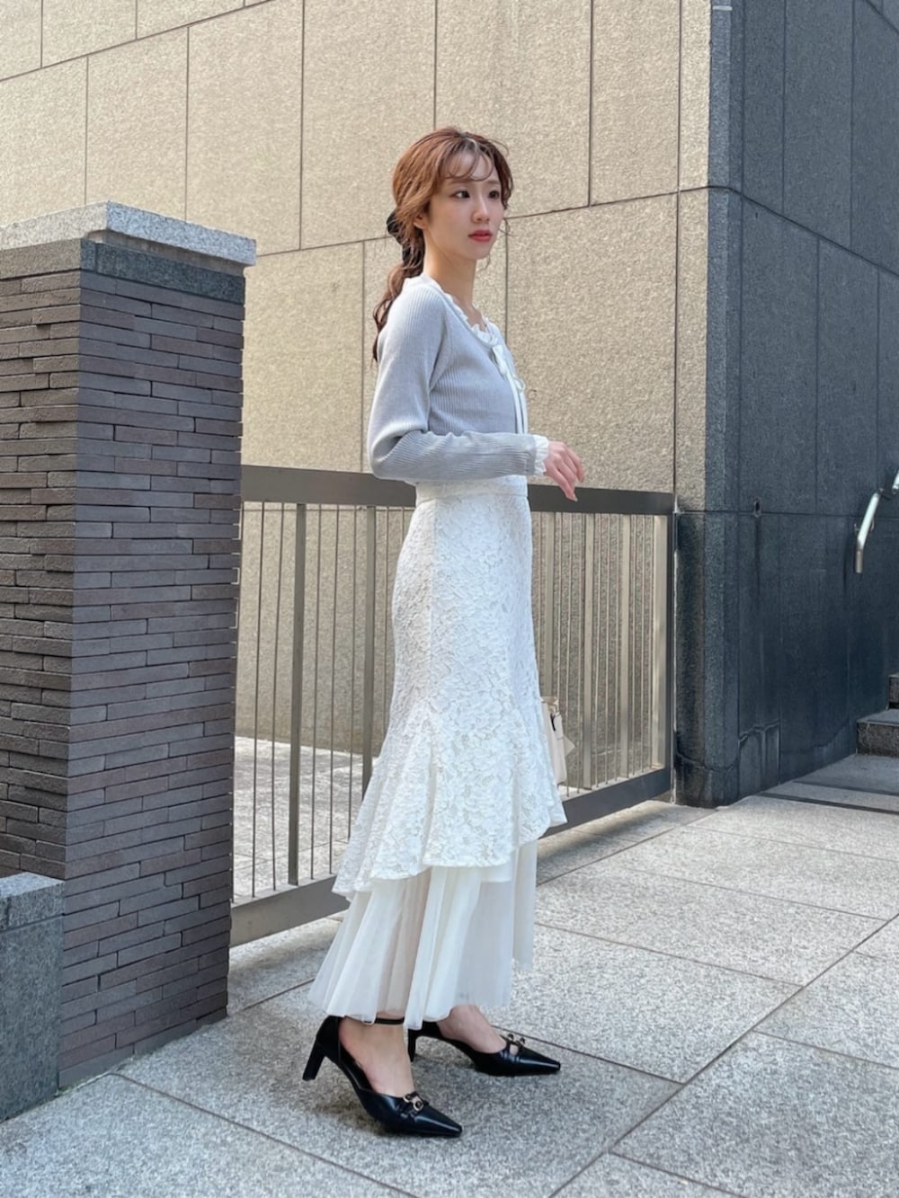 ホワイト系のショルダーバッグ、ブラック系のパンプス、グレー系のニット/セーターを着用したレディースの春コーディネートの2枚目の写真