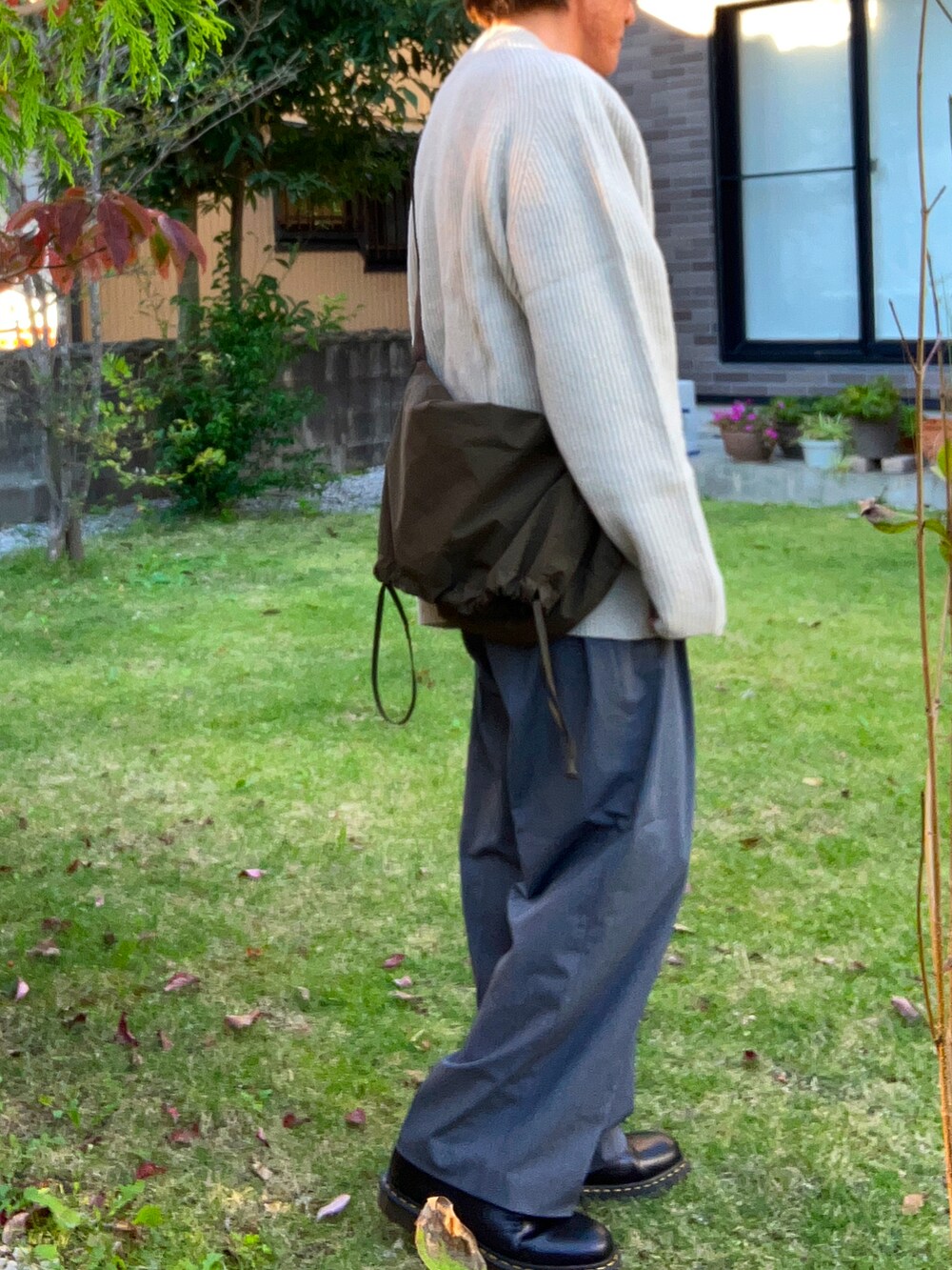 グレー系のスラックス、ベージュ系のニット/セーター、グリーン系のショルダーバッグを着用したメンズの秋コーディネートの2枚目の写真