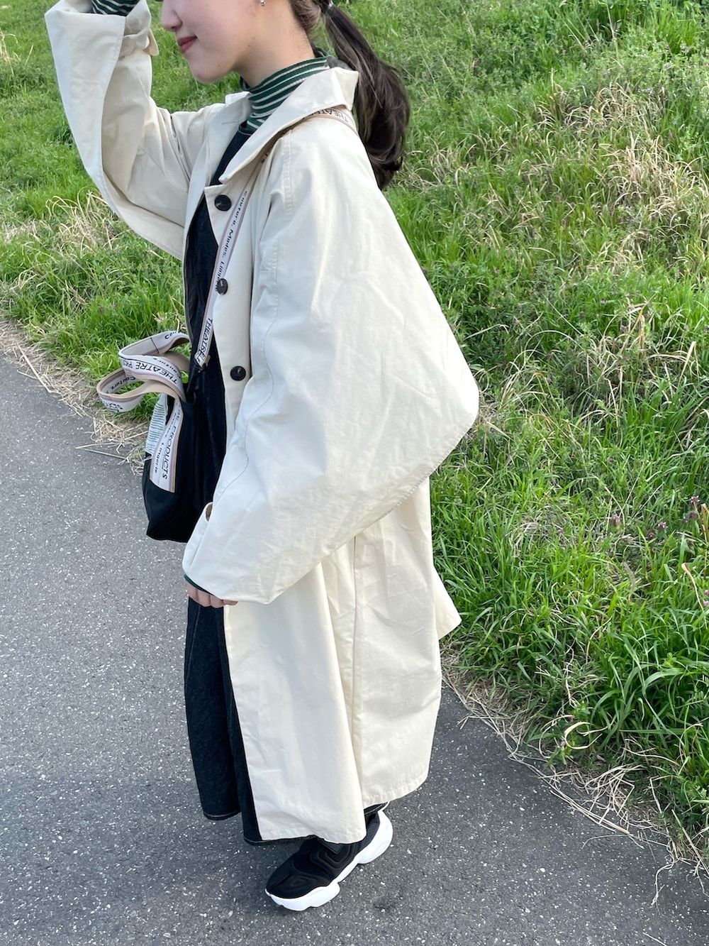 ホワイト系のステンカラーコート、ブラック系のワンピース、ブラック系のスニーカーを着用したレディースの春コーディネートの2枚目の写真