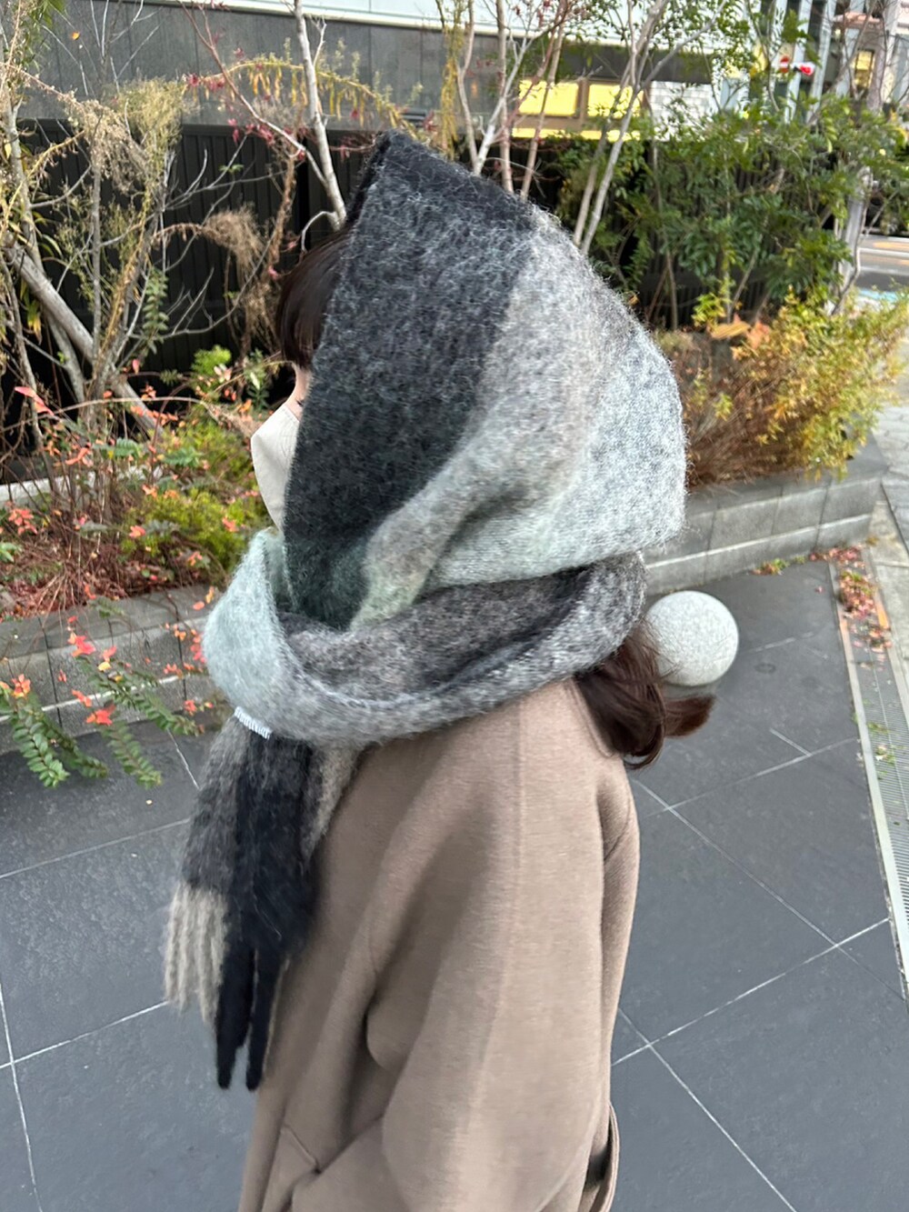 ベージュ系のステンカラーコート、グリーン系のマフラーを着用したレディースの冬コーディネートの2枚目の写真