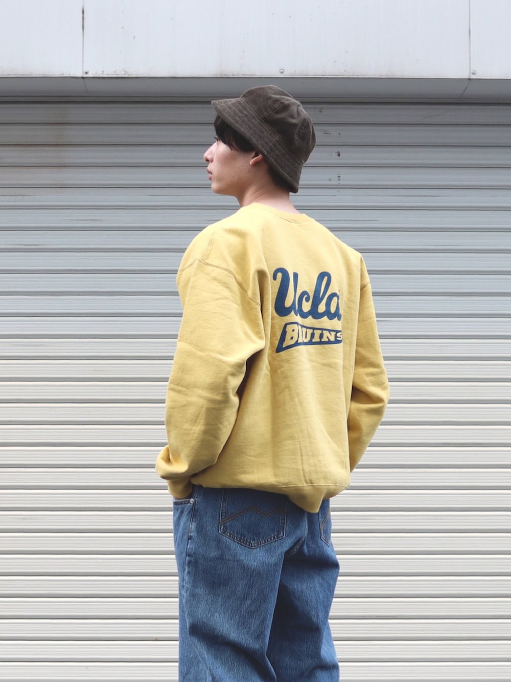 イエロー系のスウェット、ブルー系のデニムパンツ、グレー系のスニーカーを着用したメンズの冬コーディネートの2枚目の写真