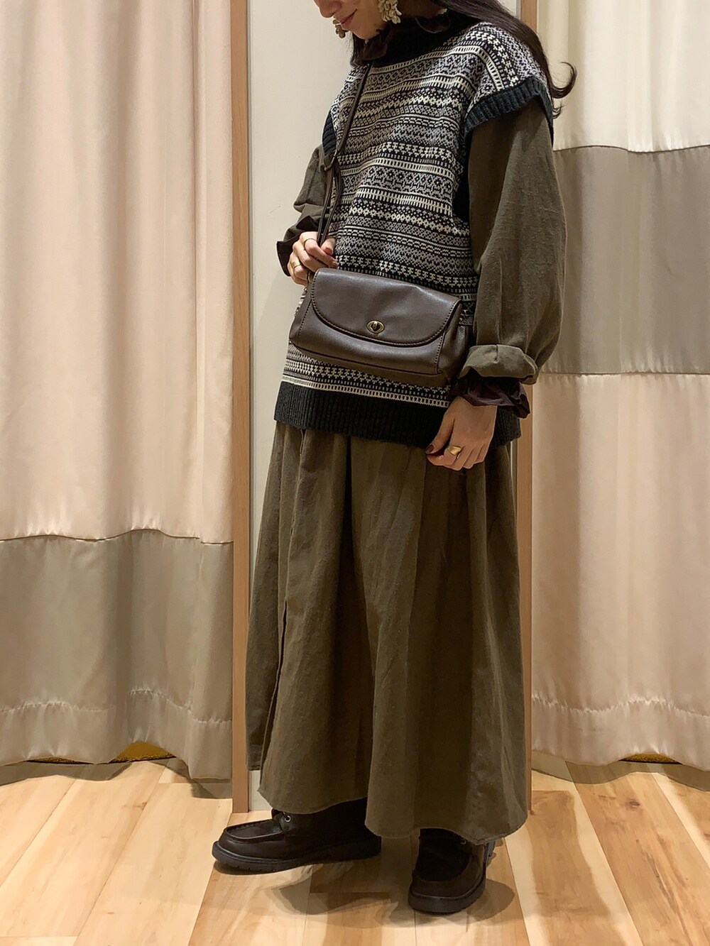 ブラック系のベスト、ブラウン系のショルダーバッグ、ブラウン系のシャツ/ブラウスを着用したレディースの秋コーディネートの2枚目の写真