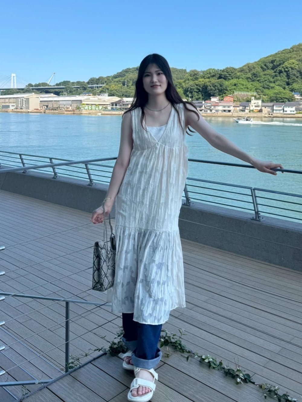 ホワイト系のワンピース、ブルー系のデニムパンツ、ホワイト系のショルダーバッグを着用したレディースの夏コーディネートの2枚目の写真