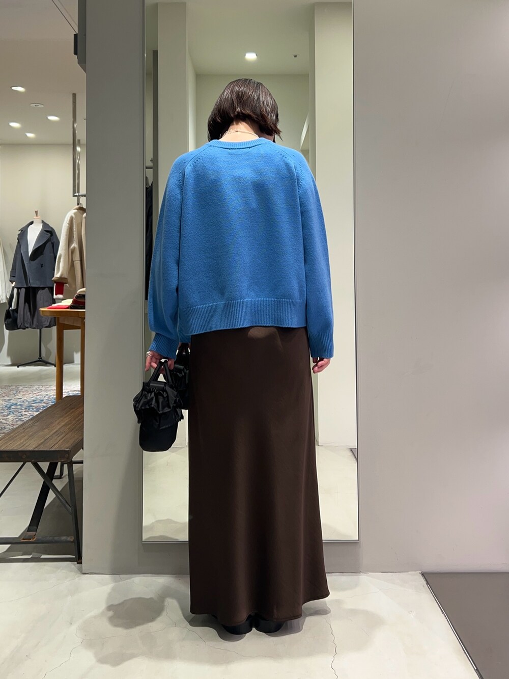 ブラウン系のスカート、ブルー系のニット/セーター、ブラック系のハンドバッグを着用したレディースの冬コーディネートの2枚目の写真