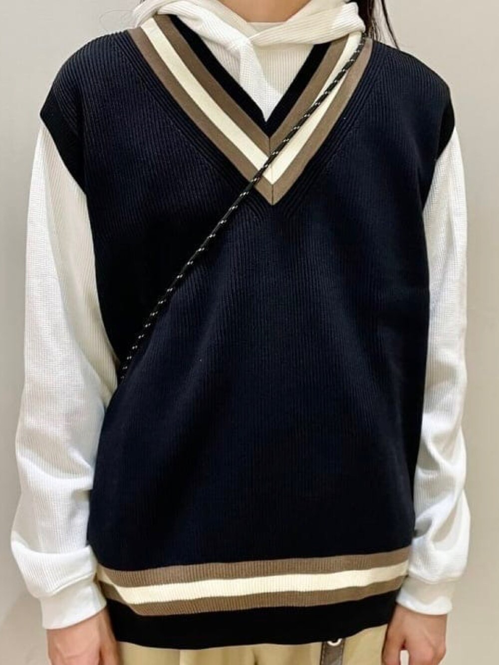 ブラック系のベスト、ホワイト系のパーカー、ベージュ系のチノパンツを着用したメンズの秋コーディネートの2枚目の写真