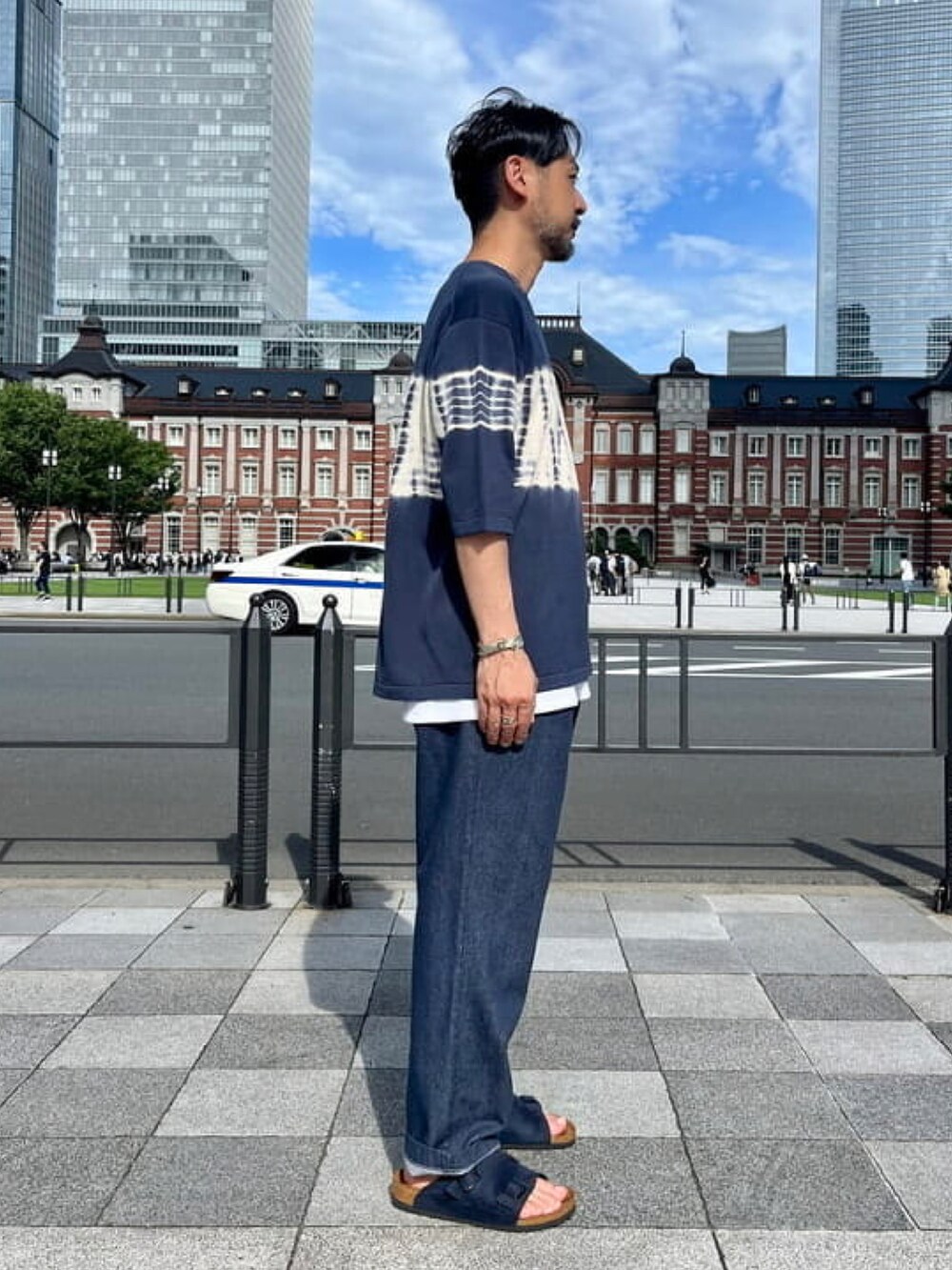 ブルー系のTシャツ/カットソー、ブルー系のデニムパンツ、ブラウン系のハンドバッグを着用したメンズの夏コーディネートの2枚目の写真