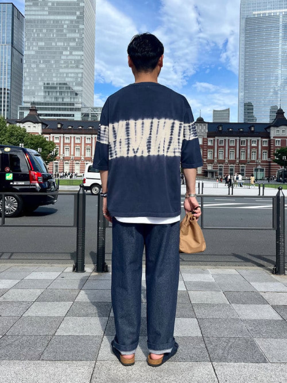 ブルー系のTシャツ/カットソー、ブルー系のデニムパンツ、ブラウン系のハンドバッグを着用したメンズの夏コーディネートの3枚目の写真