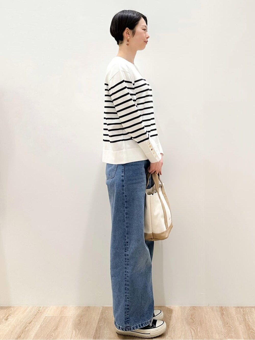 ホワイト系のニット/セーター、ブルー系のデニムパンツ、ベージュ系のトートバッグを着用したレディースの冬コーディネートの3枚目の写真