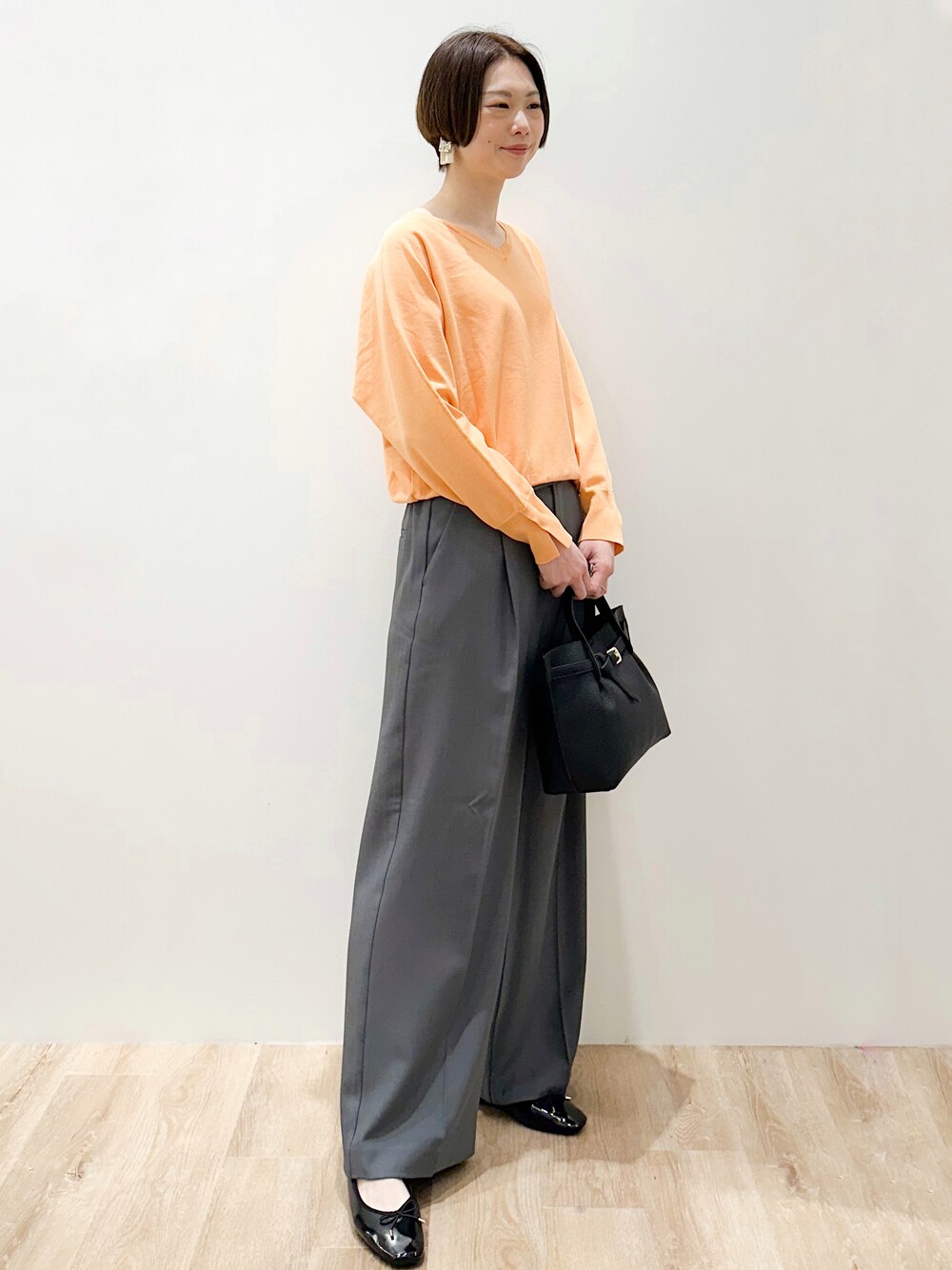 オレンジ系のニット/セーター、グレー系のその他パンツ、ブラック系のトートバッグを着用したレディースの春コーディネートの5枚目の写真