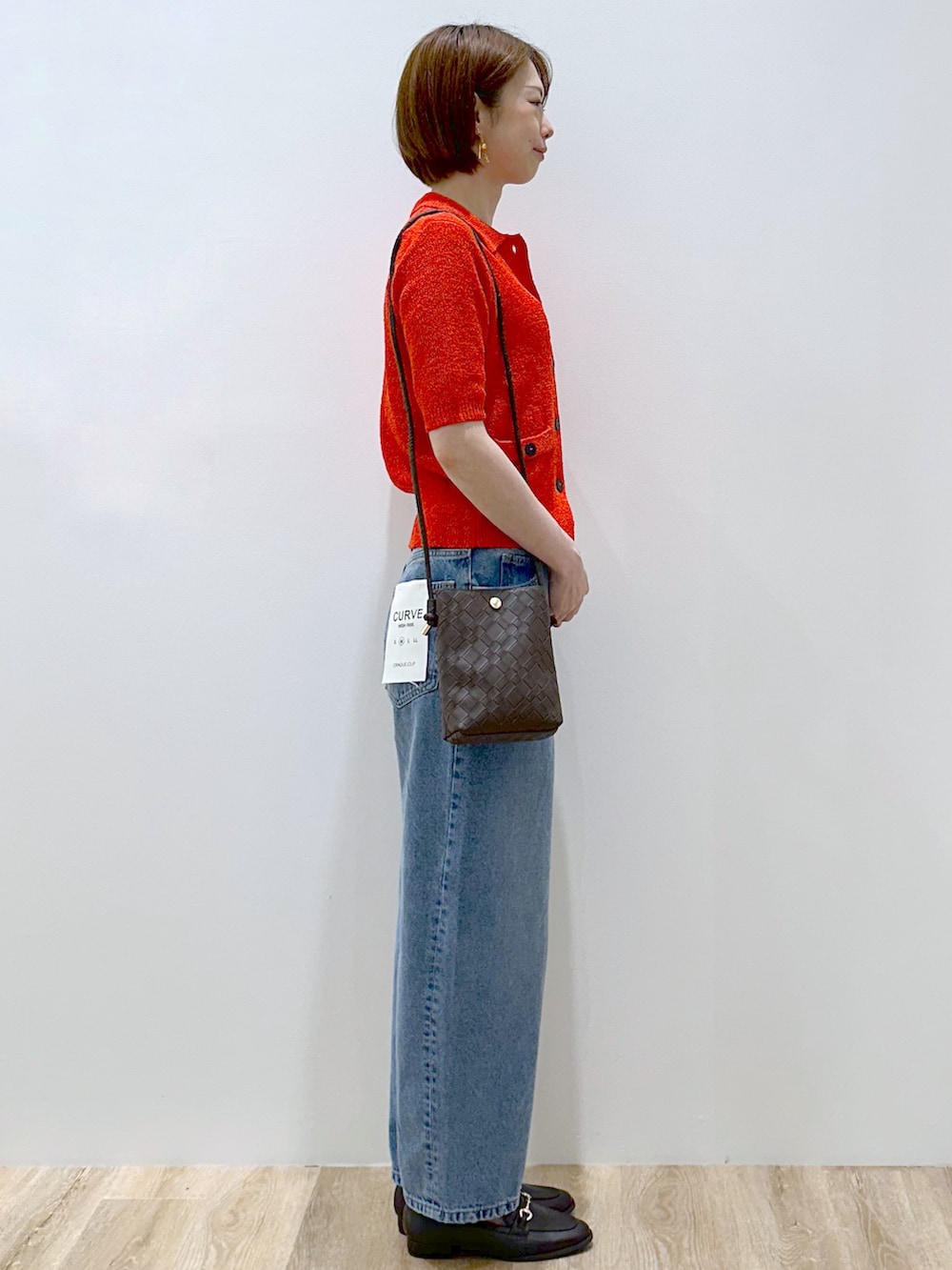 レッド系のカーディガン/ボレロ、ブルー系のデニムパンツ、ブラウン系のショルダーバッグを着用したレディースの夏コーディネートの4枚目の写真