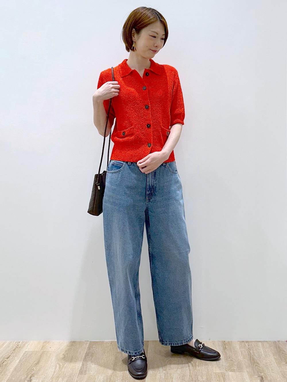 レッド系のカーディガン/ボレロ、ブルー系のデニムパンツ、ブラウン系のショルダーバッグを着用したレディースの夏コーディネートの3枚目の写真