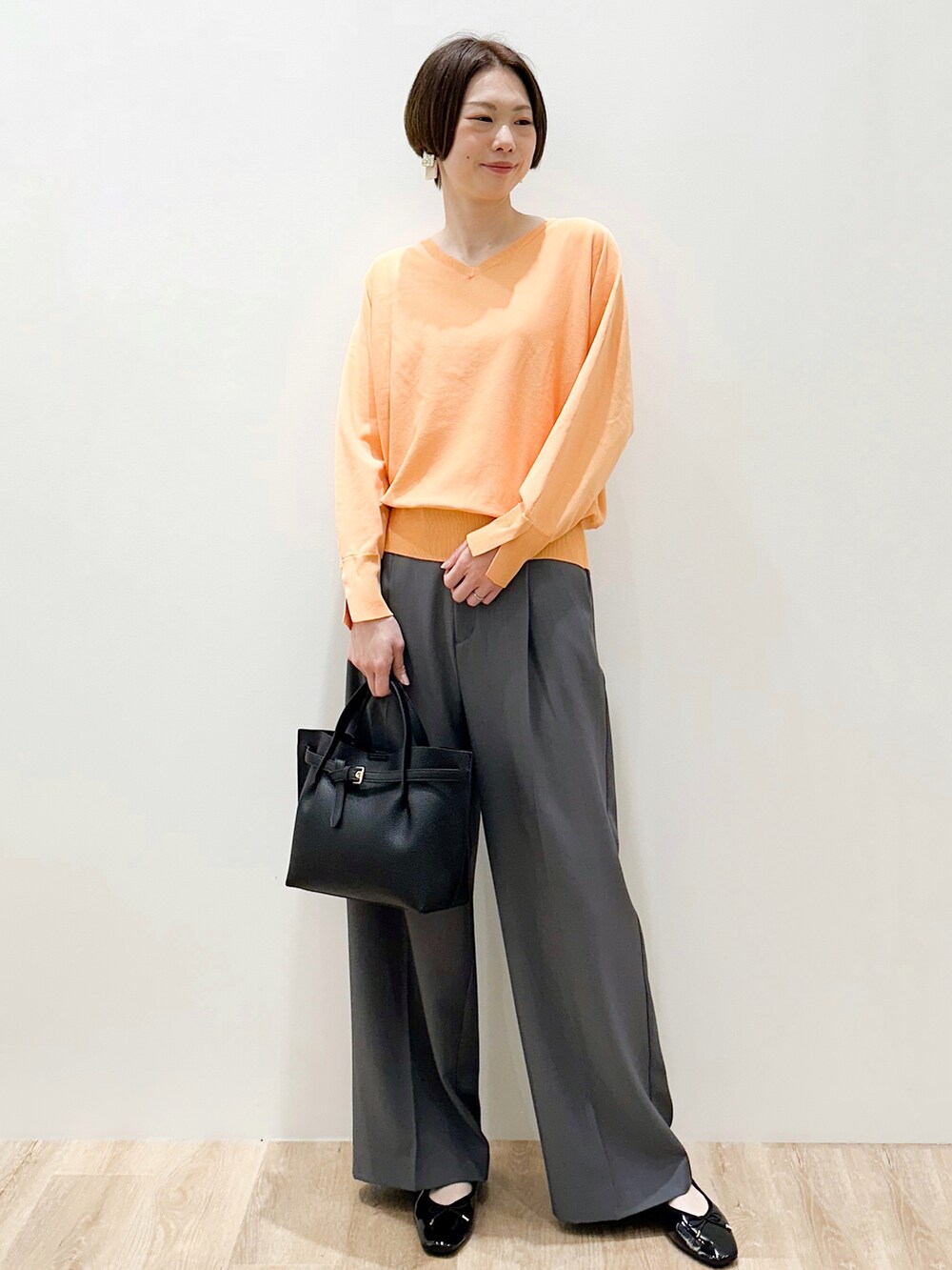 オレンジ系のニット/セーター、グレー系のその他パンツ、ブラック系のトートバッグを着用したレディースの春コーディネートの2枚目の写真