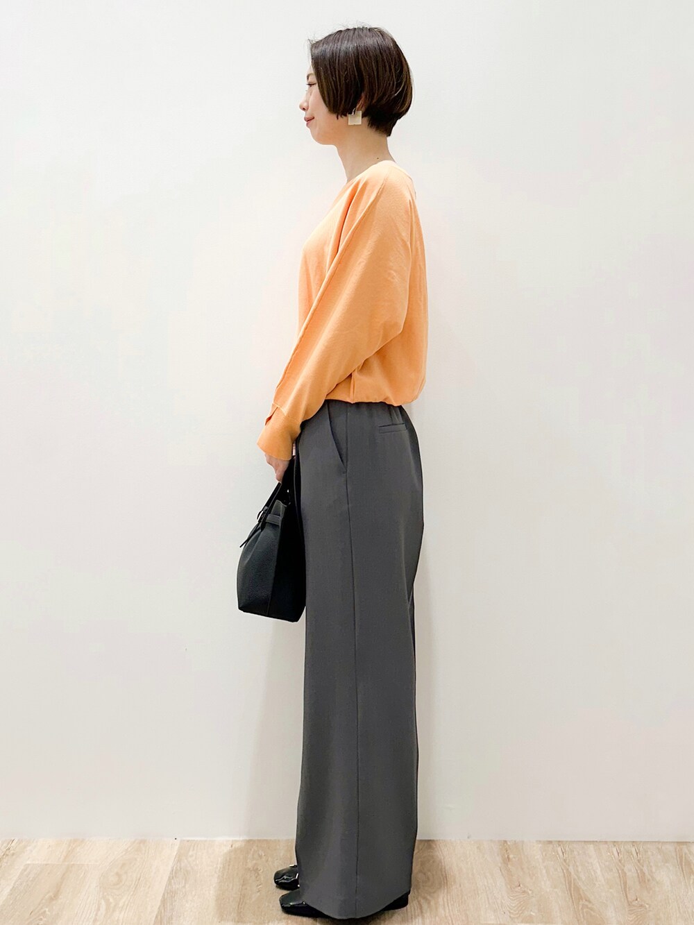 オレンジ系のニット/セーター、グレー系のその他パンツ、ブラック系のトートバッグを着用したレディースの春コーディネートの3枚目の写真