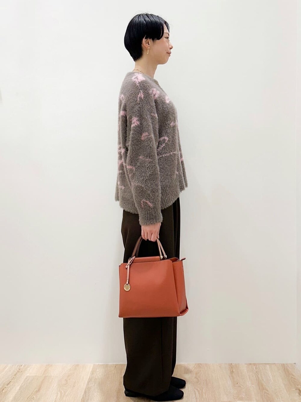 グレー系のニット/セーター、ブラウン系のその他パンツ、オレンジ系のトートバッグを着用したレディースの冬コーディネートの2枚目の写真