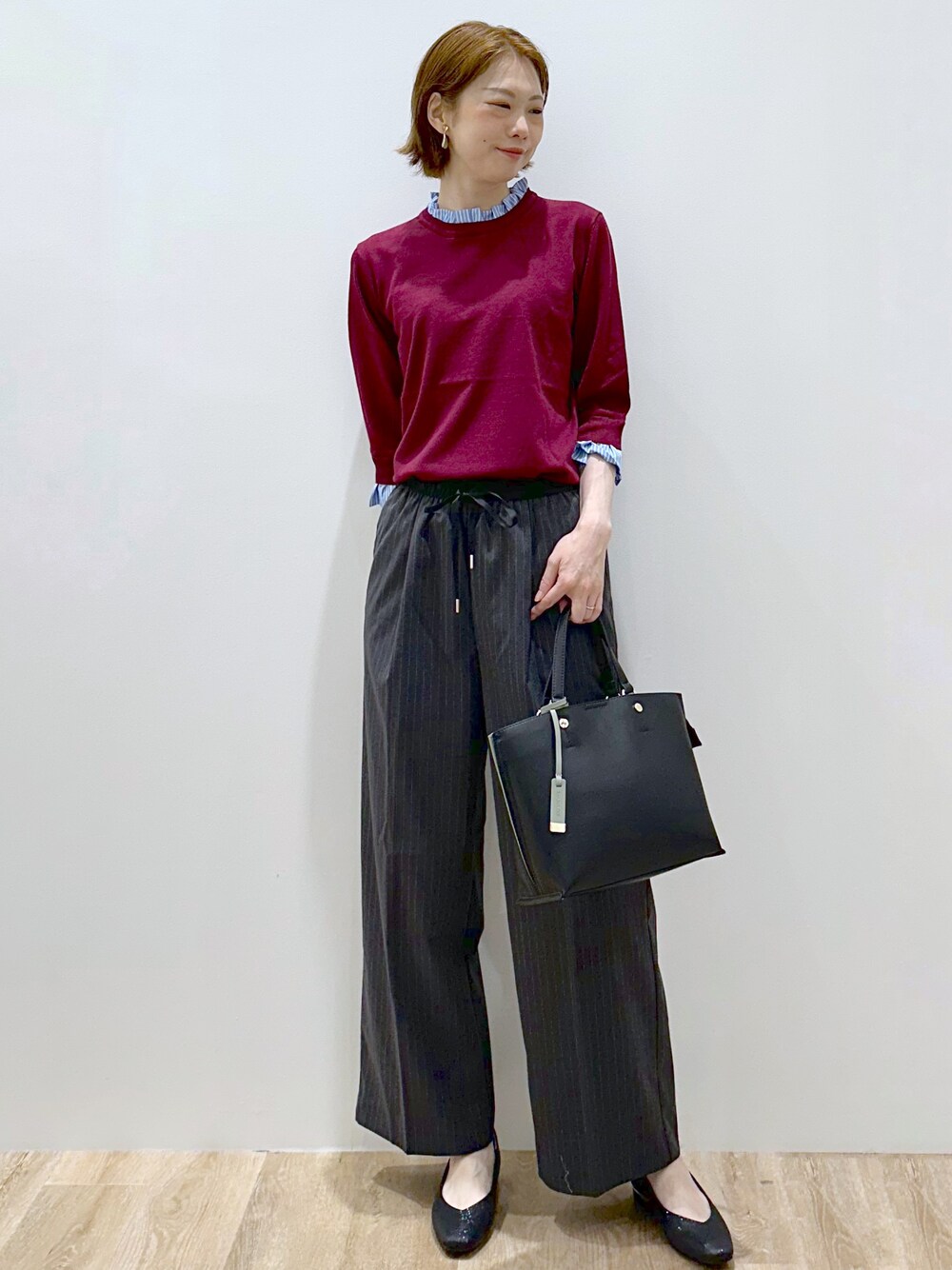 レッド系のニット/セーター、グレー系のその他パンツ、ブラック系のトートバッグを着用したレディースの秋コーディネートの2枚目の写真