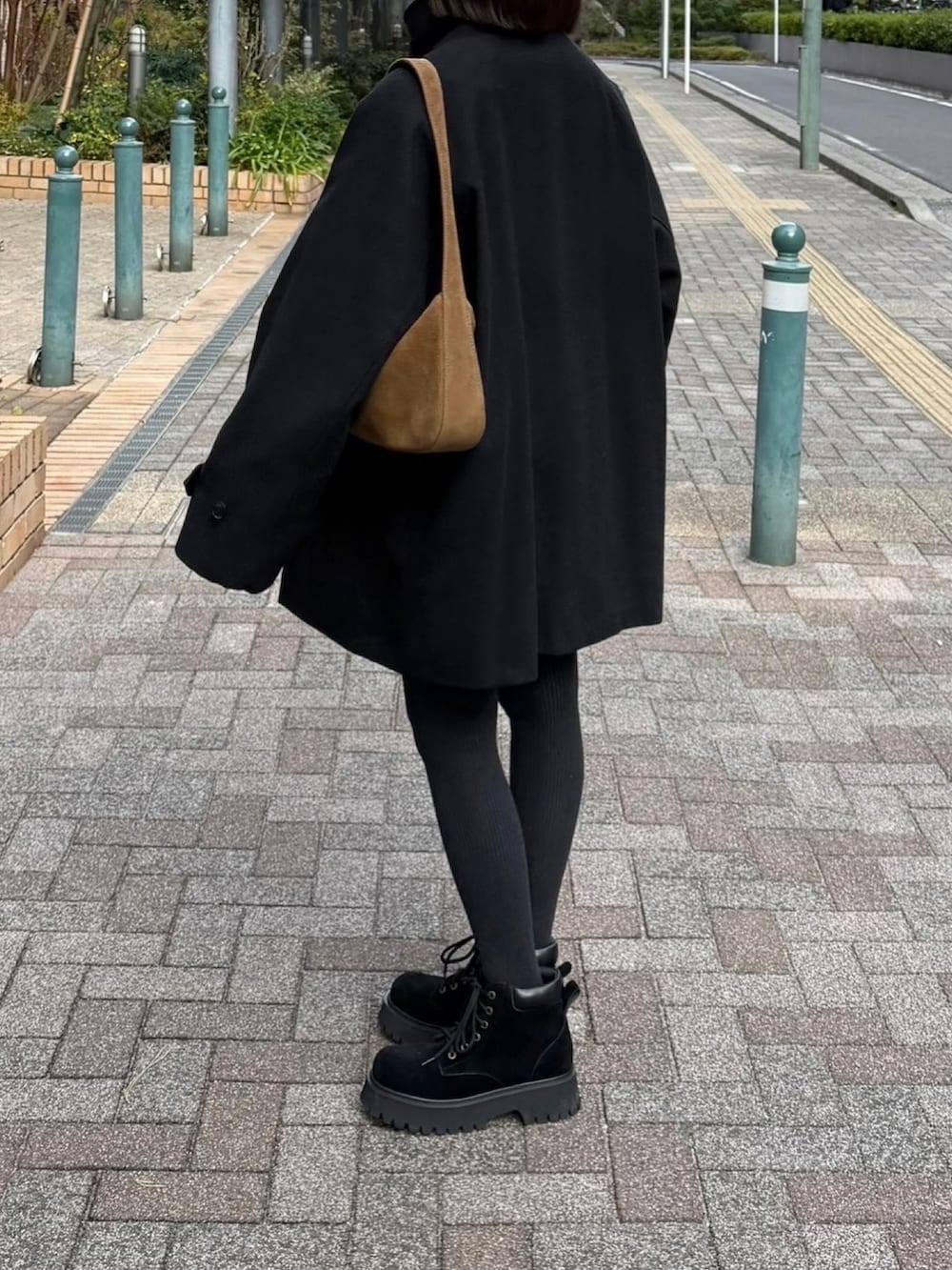 ブラック系のステンカラーコート、イエロー系のハンドバッグ、ブラック系のブーツを着用したレディースの冬コーディネートの2枚目の写真