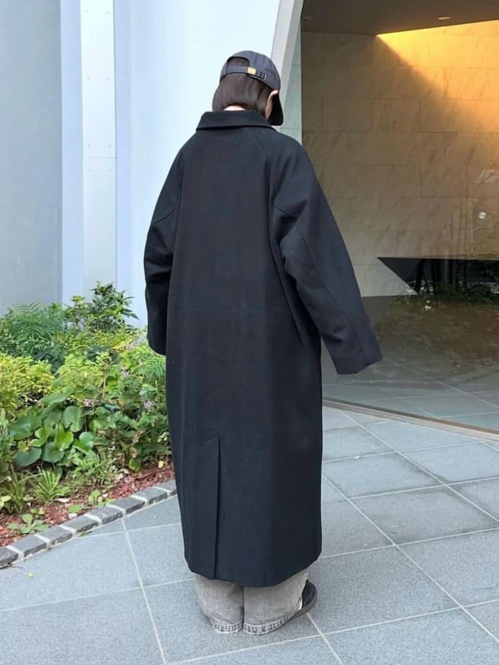 ブラック系のステンカラーコート、グレー系のデニムパンツ、ブラック系のスニーカーを着用したレディースの秋コーディネートの4枚目の写真