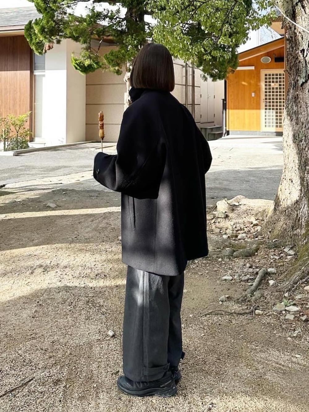 ブラック系のステンカラーコート、グレー系のスラックス、ブラック系のスニーカーを着用したレディースの冬コーディネートの2枚目の写真