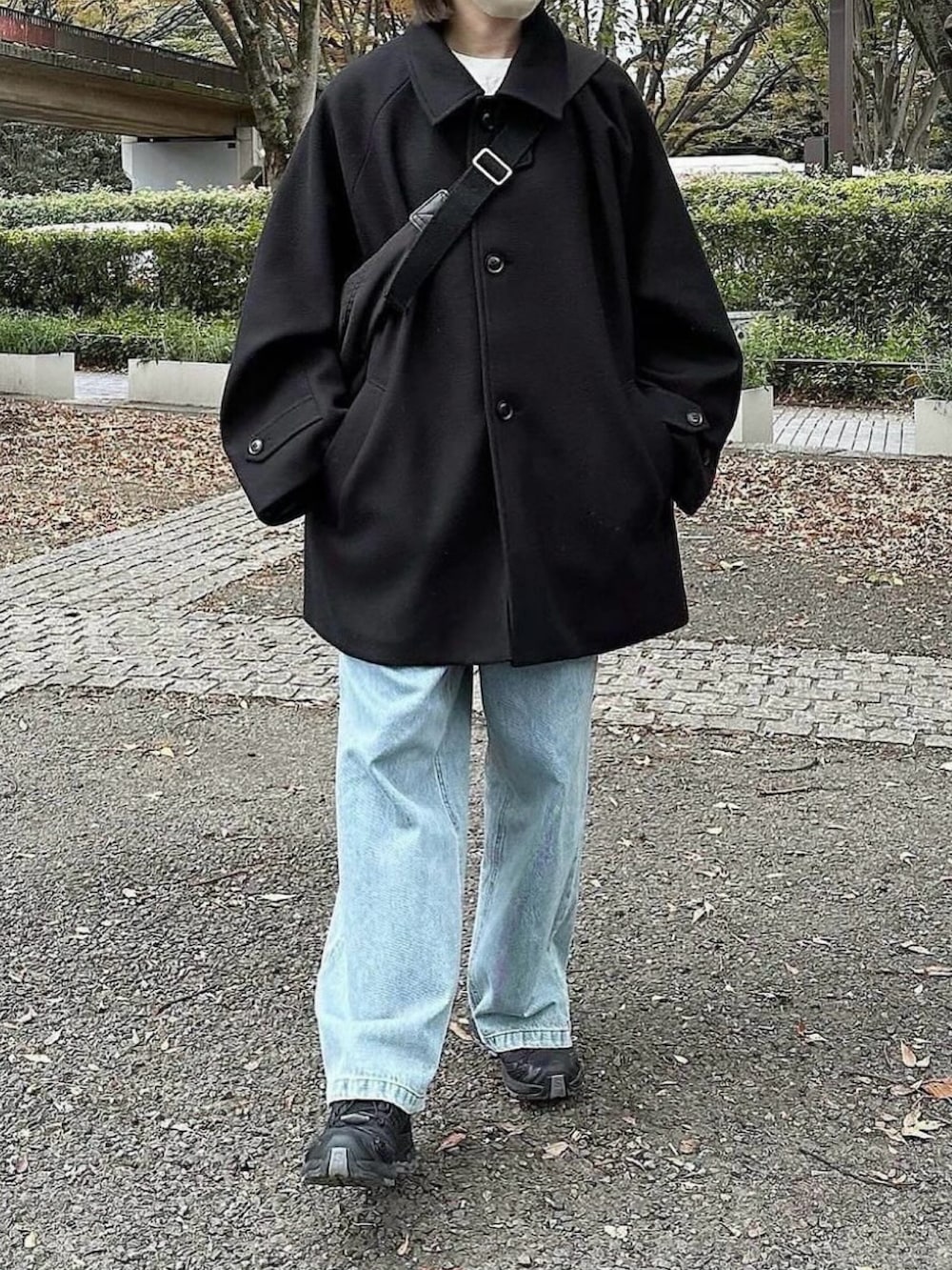 ブラック系のステンカラーコート、ブラック系のスニーカー、ブルー系のデニムパンツを着用したレディースの冬コーディネートの2枚目の写真