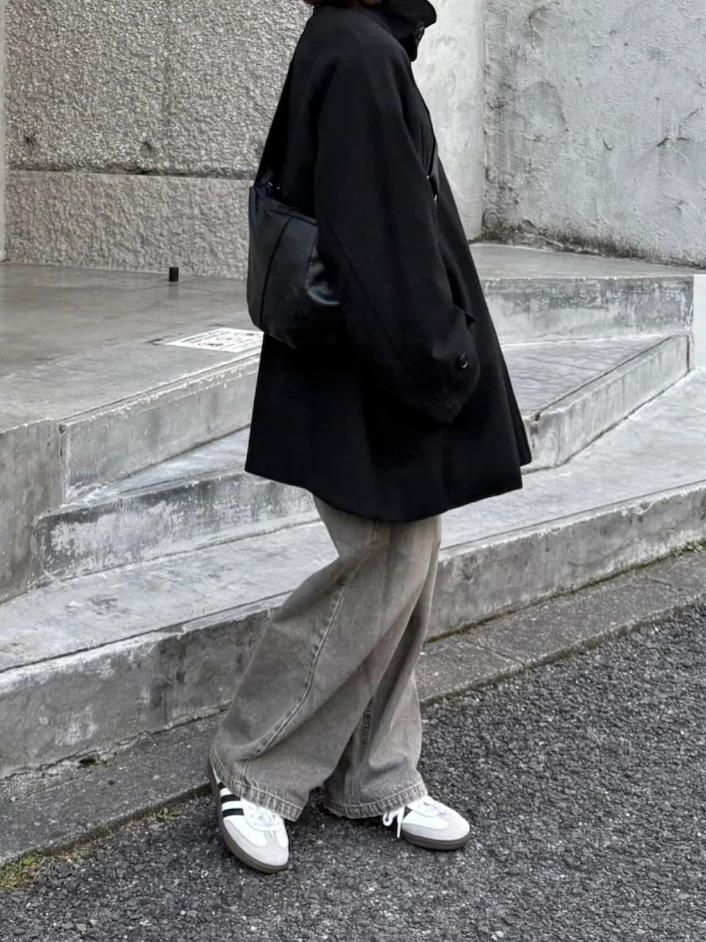 ブラック系のステンカラーコート、グレー系のデニムパンツ、ホワイト系のスニーカーを着用したレディースの冬コーディネートの2枚目の写真