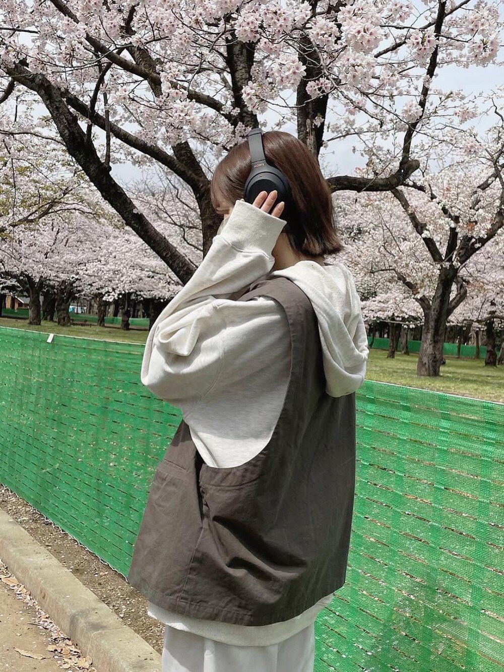 グレー系のベスト、グレー系のパーカー、ホワイト系のチノパンツを着用したレディースの春コーディネートの2枚目の写真