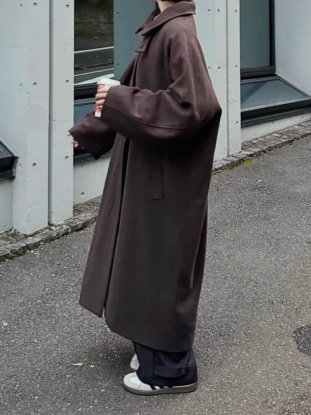 ブラウン系のステンカラーコート、ブラック系のスラックス、ホワイト系のスニーカーを着用したレディースの冬コーディネートの2枚目の写真