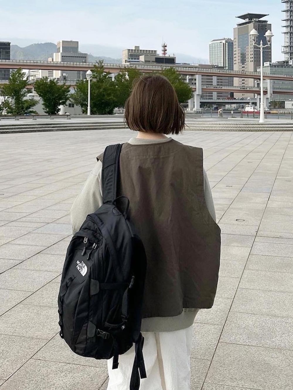 グレー系のベスト、ホワイト系のその他パンツ、ブラック系のバックパック/リュックを着用したレディースの春コーディネートの2枚目の写真