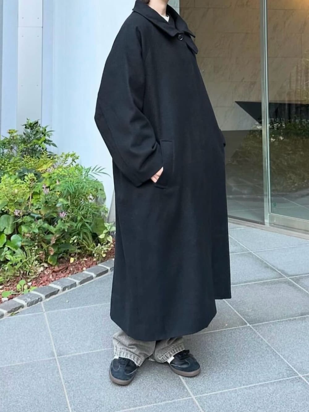 ブラック系のステンカラーコート、グレー系のデニムパンツ、ブラック系のスニーカーを着用したレディースの秋コーディネートの3枚目の写真