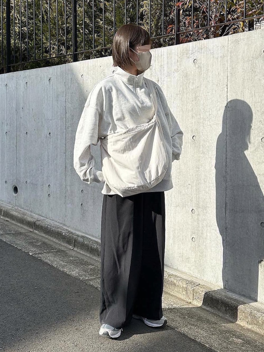 グレー系のスウェット、ブラック系のスラックス、ホワイト系のショルダーバッグを着用したレディースの冬コーディネートの2枚目の写真