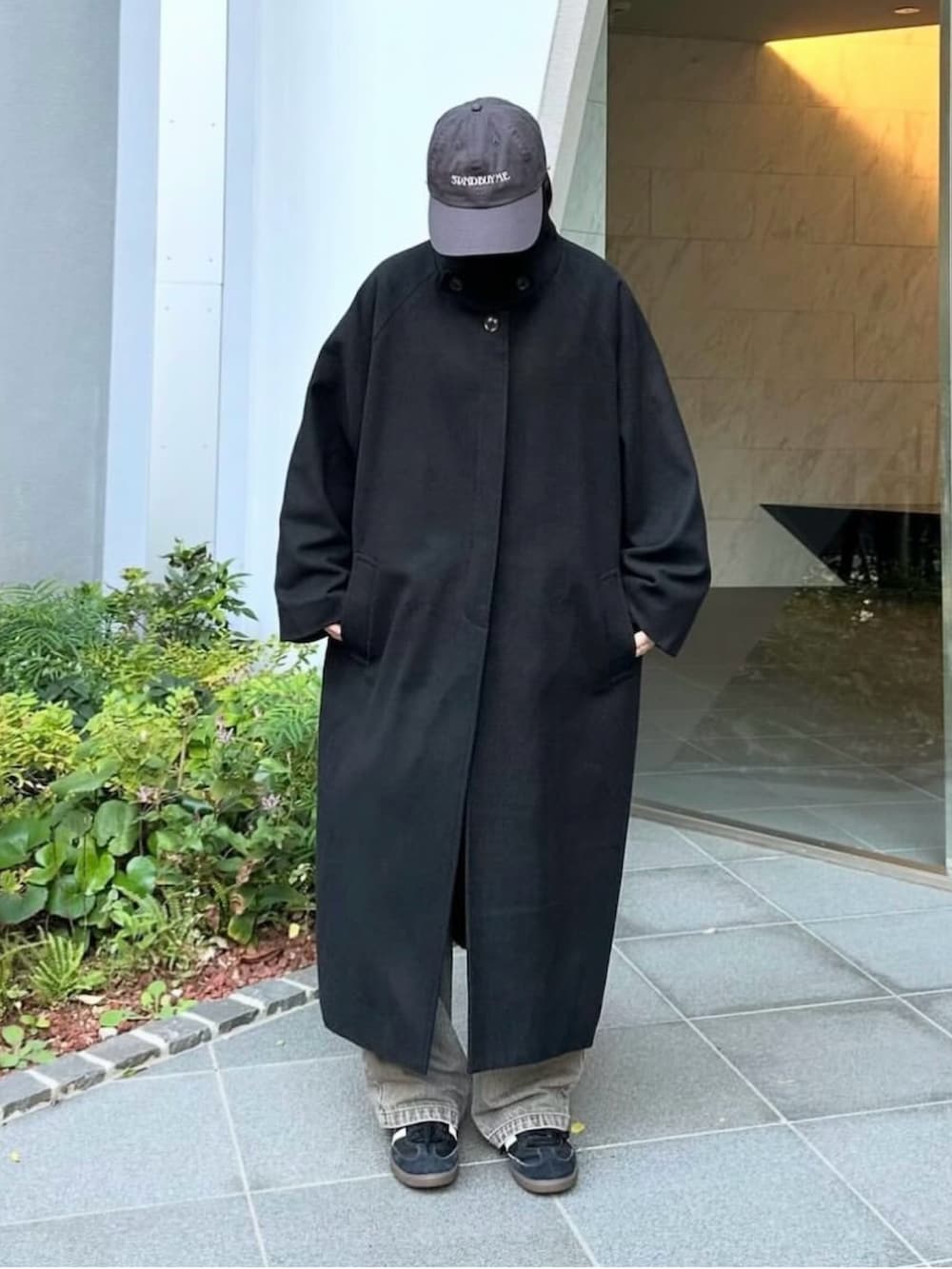 ブラック系のステンカラーコート、グレー系のデニムパンツ、ブラック系のスニーカーを着用したレディースの秋コーディネートの2枚目の写真