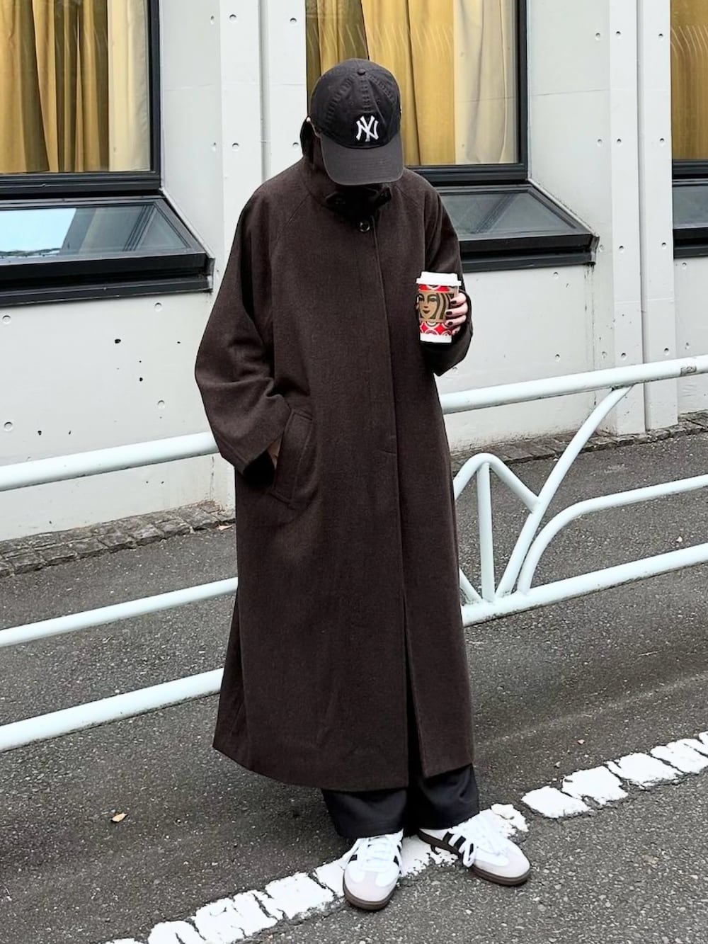 ブラウン系のステンカラーコート、ブラック系のスラックス、ホワイト系のスニーカーを着用したレディースの秋コーディネートの2枚目の写真