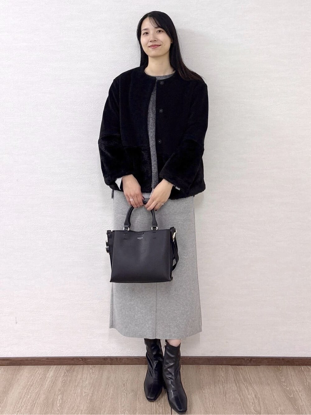 ブラック系のノーカラーコート、グレー系のニット/セーター、ホワイト系のTシャツ/カットソーを着用したレディースの冬コーディネートの2枚目の写真